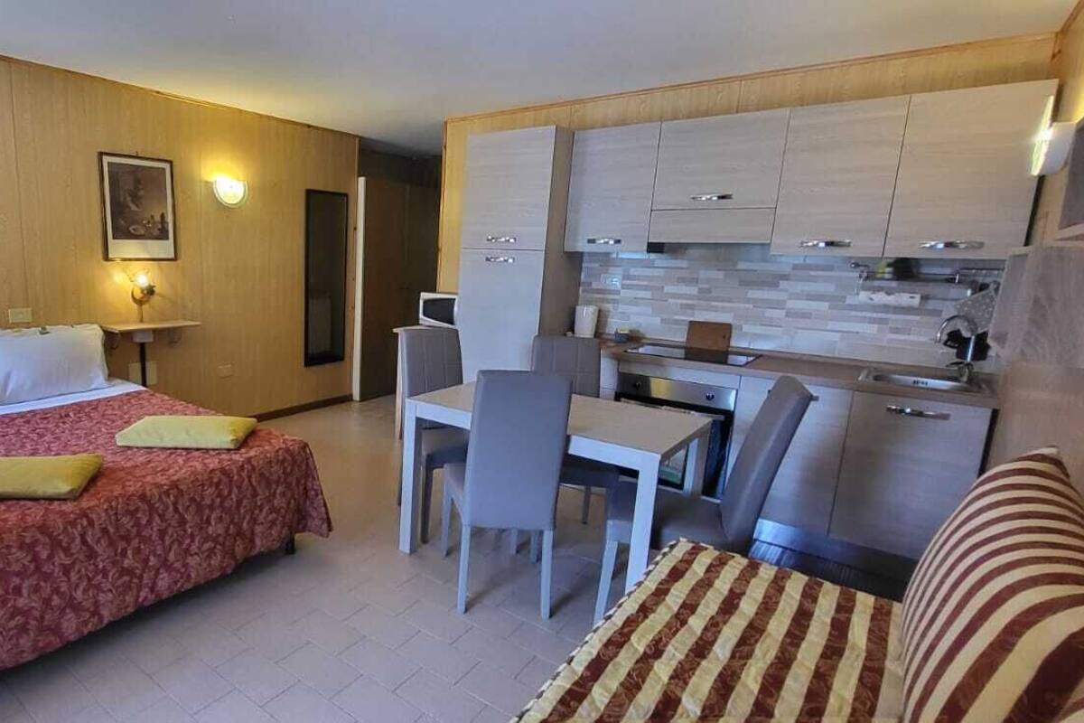 A compact hotel room with a bed, a small kitchenette, a dining area, and a sofa.
