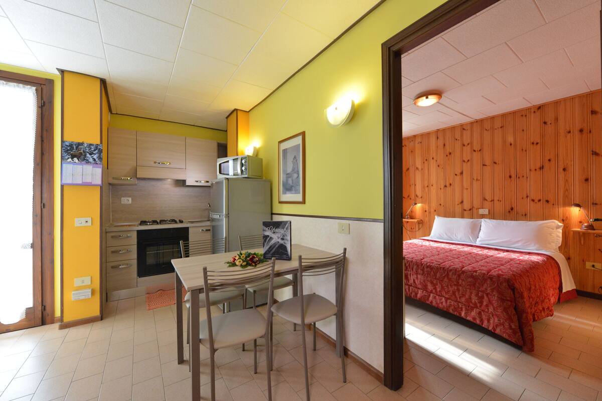 A compact room with a kitchenette, a dining area, and a bed.