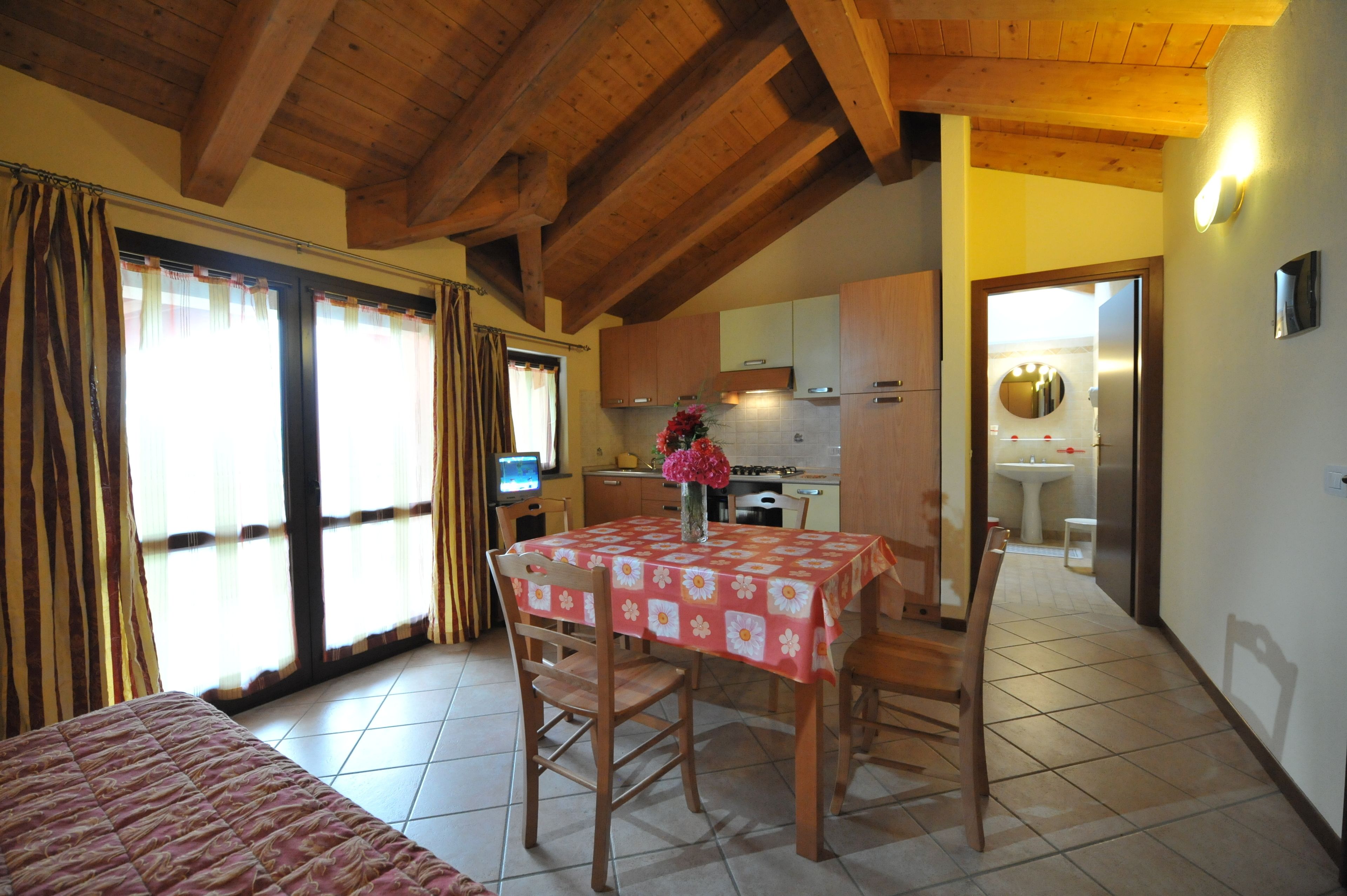 A room with a dining table, chairs, a bed, a TV, and a kitchen area.