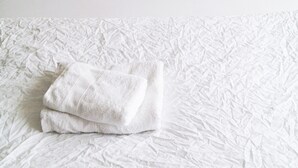 Un lit bien fait, avec une couette blanche à texture et une serviette blanche pliée posée dessus.
