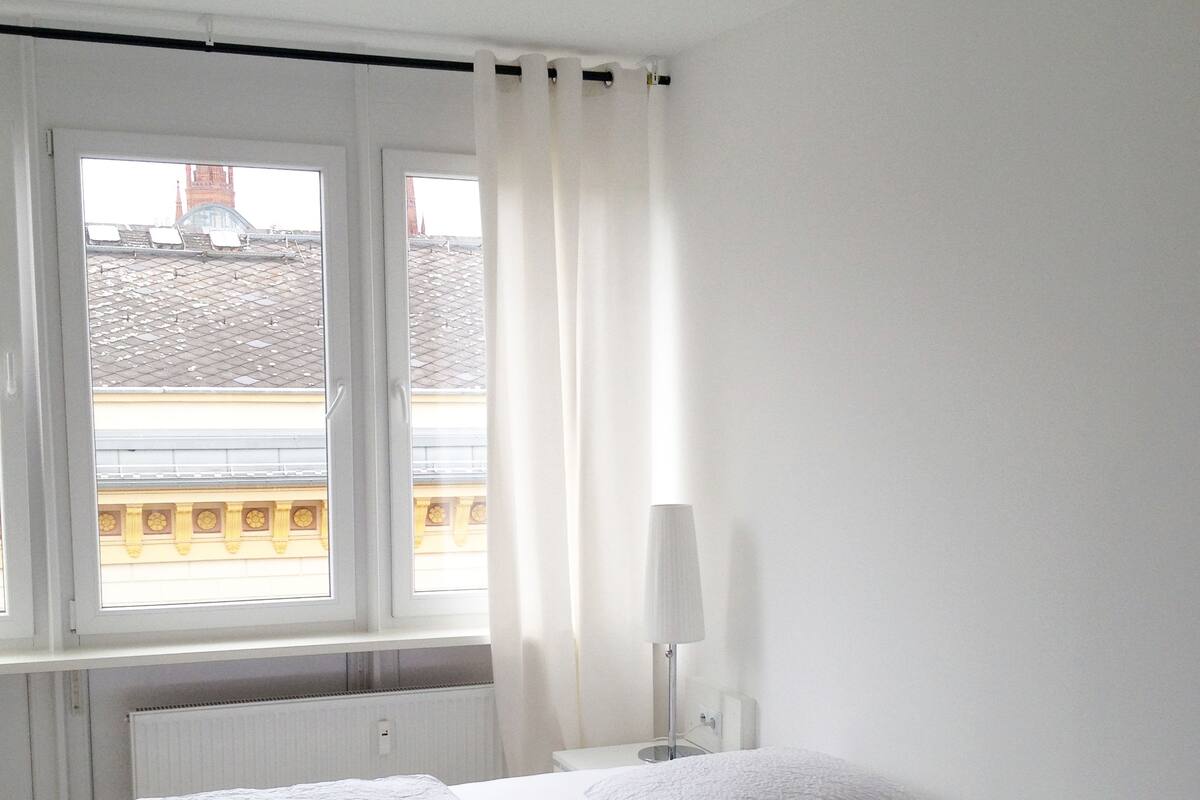 Un dormitorio minimalista con cama, mesita de noche y ventana con cortinas.