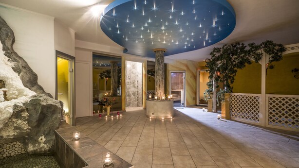 Un espace de détente avec un mur en pierre, un pilier circulaire orné de bougies et un plafond décoré de lumières en forme d’étoiles.