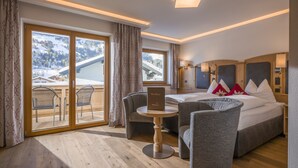 Une chambre d’hôtel avec un lit, deux fauteuils, une petite table et une vue sur des montagnes enneigées, visible à travers de grandes fenêtres.