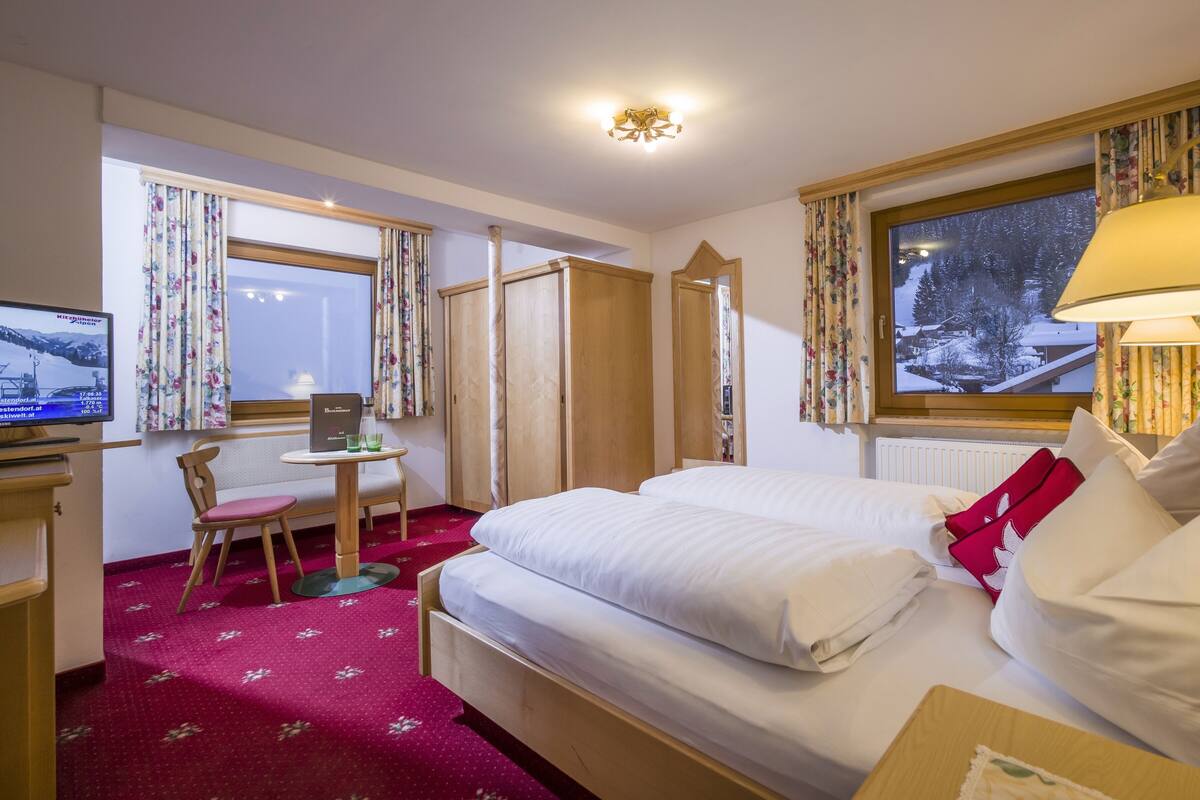 A hotel room with a bed, a desk with a chair, a television, and a window with a view of a snowy landscape.