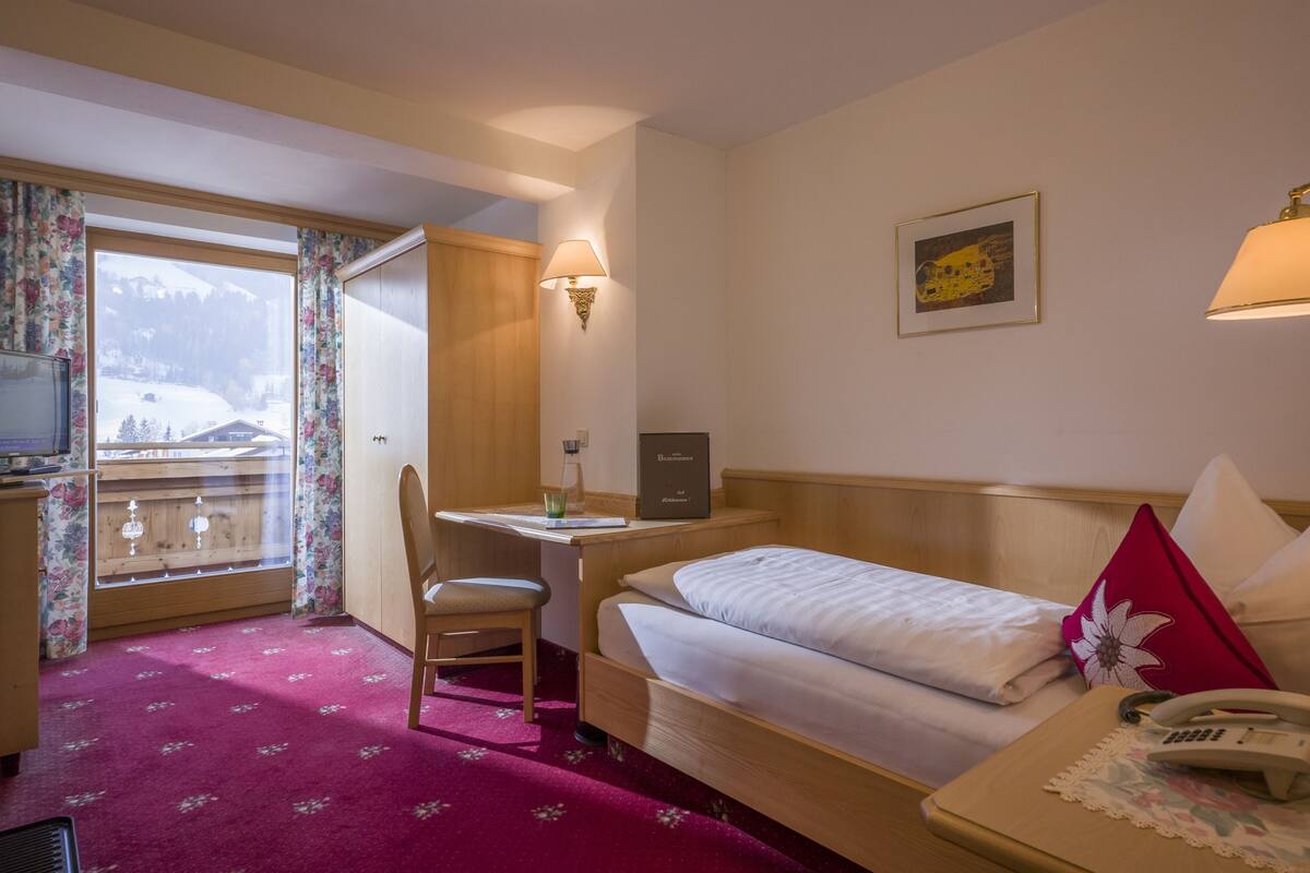 A hotel room with a bed, desk, chair, and a window with a view of a snowy landscape.