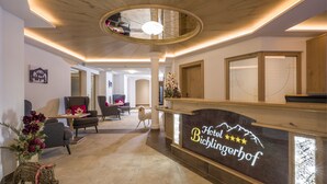 Un espace d’accueil d’hôtel avec un comptoir de réception en bois, des sièges confortables et un vase décoratif rempli de fleurs.