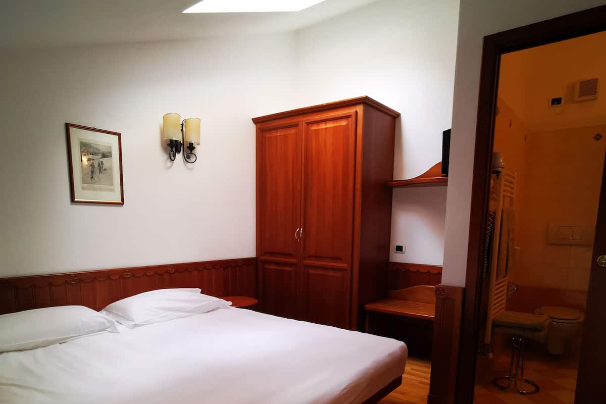 Ein Hotelzimmer mit einem großen Bett, einem Kleiderschrank, einem kleinen Tisch und einem durch eine offene Tür einsehbaren Badezimmer.