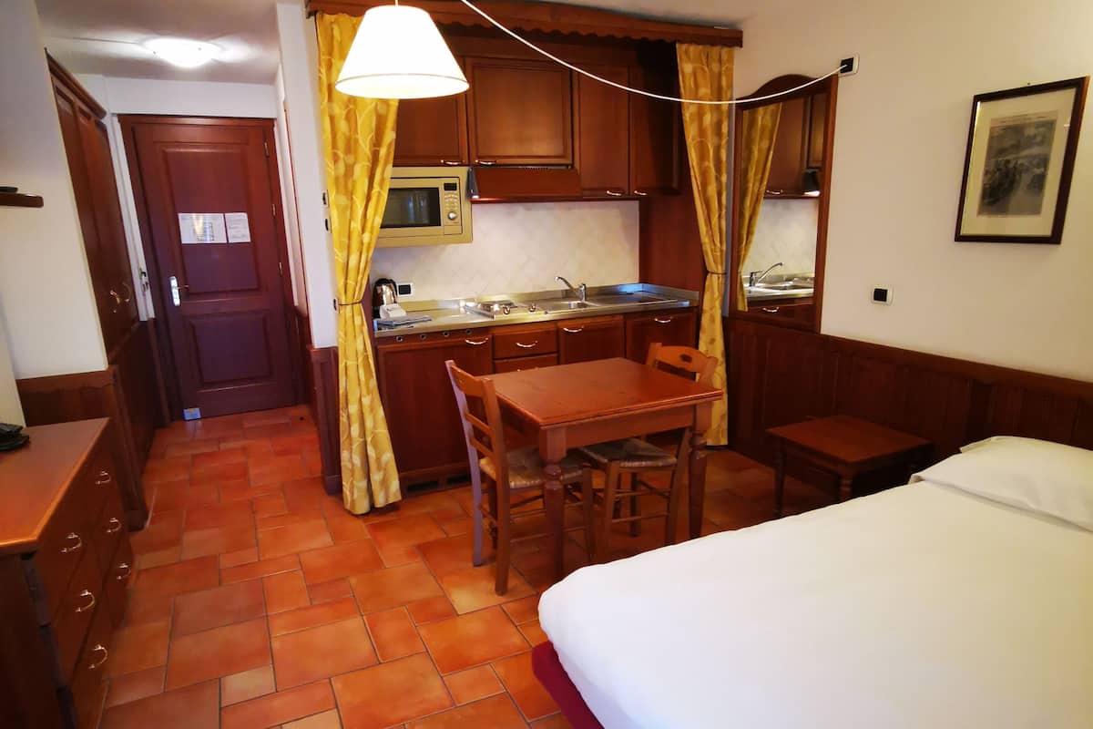 Ein kompaktes Hotelzimmer mit Küchenzeile, einem Bett, einem Schreibtisch und einem Stuhl.