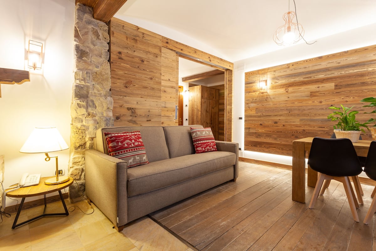 Ein gemütlicher Wohnbereich mit einer Couch, einem kleinen Tisch mit Lampe sowie einem Esstisch mit Stühlen.
