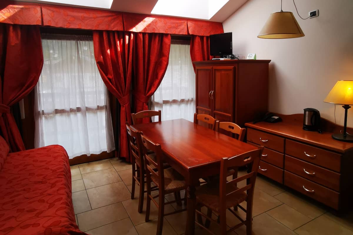 Ein Zimmer mit Esstisch aus Holz, Stühlen, einem Bett mit roter Bettwäsche, einem Fernseher, einer Lampe und Dachfenstern.