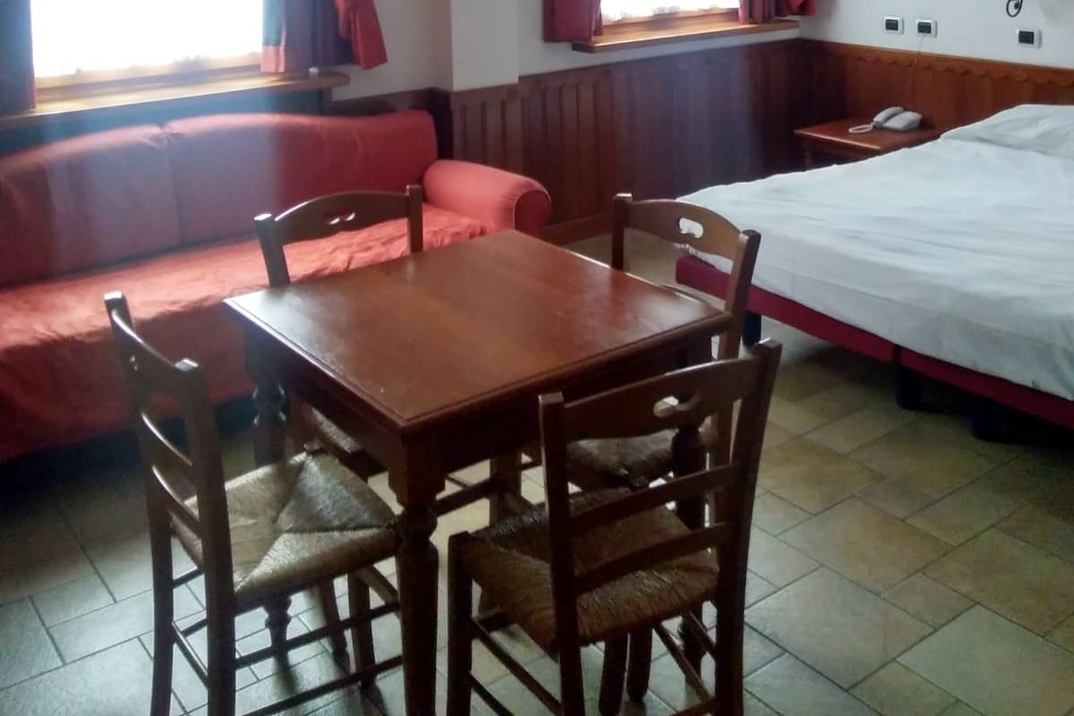 Ein Zimmer mit Holztisch und Stühlen, einem Bett, einer Bank und einem Fenster mit Vorhängen.