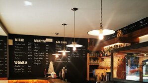 A bar area with a wooden counter, stools, hanging lights, and a menu on the wall. - Residence Le Grand Chalet (Courmayeur)
