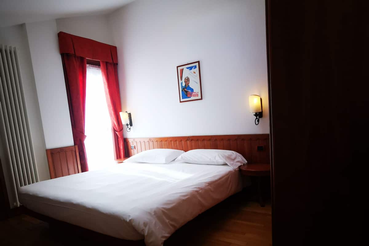 Ein Schlafzimmer mit einem Bett, einer Deckenleuchte, einer Wandlampe und einem Fenster mit Vorhängen.