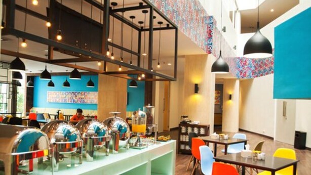 A modern dining area with a buffet setup, multiple seating arrangements, and a high ceiling with exposed beams. - idoop Hotel Lombok (Mataram)