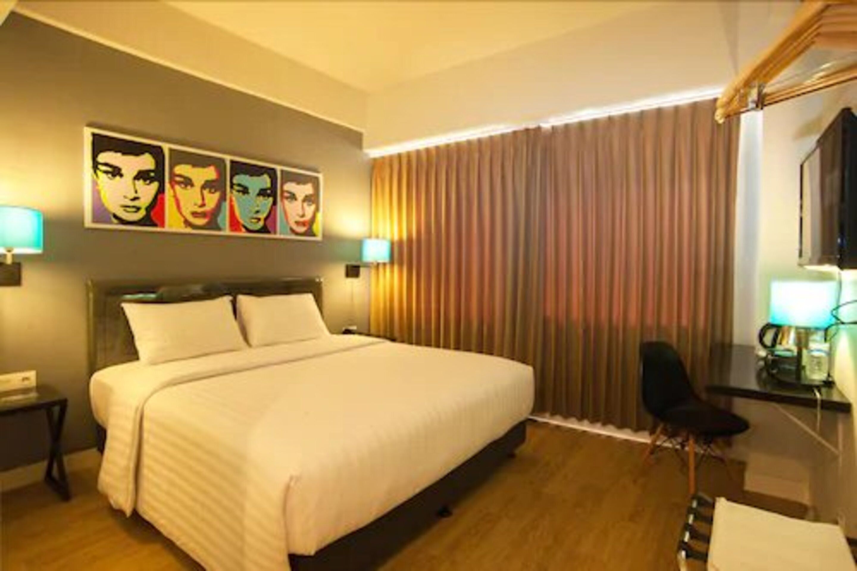 A hotel room with a large bed, a desk with a chair, and a window with curtains.