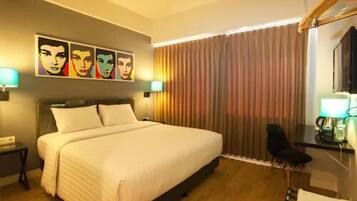 A hotel room with a large bed, a desk with a chair, and a window with curtains.