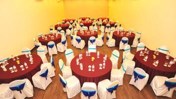 A conference room with multiple round tables, each with chairs covered in white and blue sashes. Tables are set with water bottles and glasses.