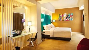 A hotel room with a bed, desk, chair, and a colorful artwork on the wall. - idoop Hotel Lombok (Mataram)