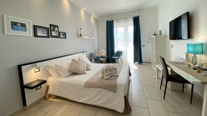 Habitación de hotel con cama, escritorio, silla, televisión y vistas al exterior.