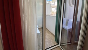 Vista a través de un ventanal corredero hacia un balcón con una silla blanca y una mesita.