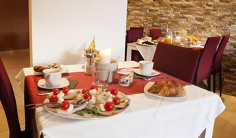 Una mesa de desayuno con cruasanes, un plato de tomates y mozzarella, una vela y un recipiente con fruta.