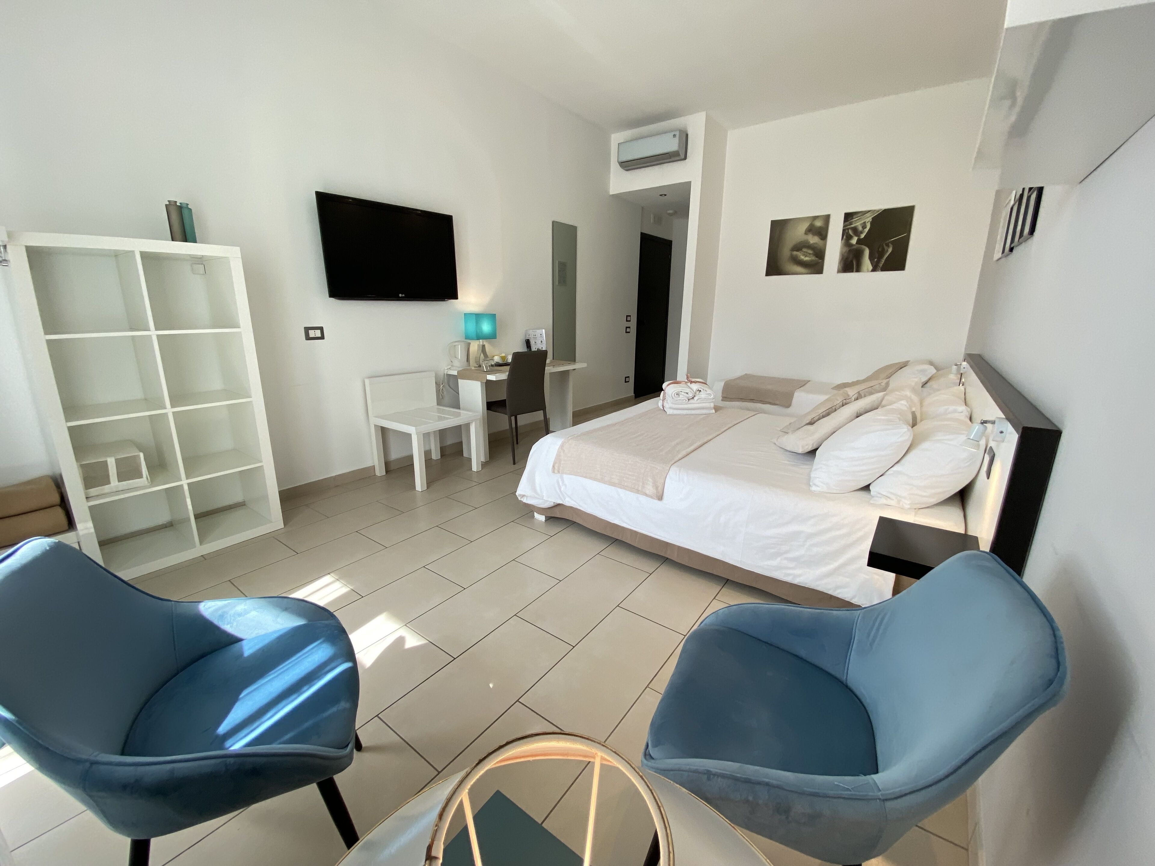 Habitación de hotel con cama, dos sillas azules, un escritorio con silla, un armario, un televisor y un aire acondicionado instalado en la pared.