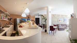 Una cocina moderna con una isla central, zona de comedor con sillas y sala de estar con sofá.