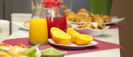 Una mesa de desayuno con jugo de naranja, una bebida roja y pastelería.