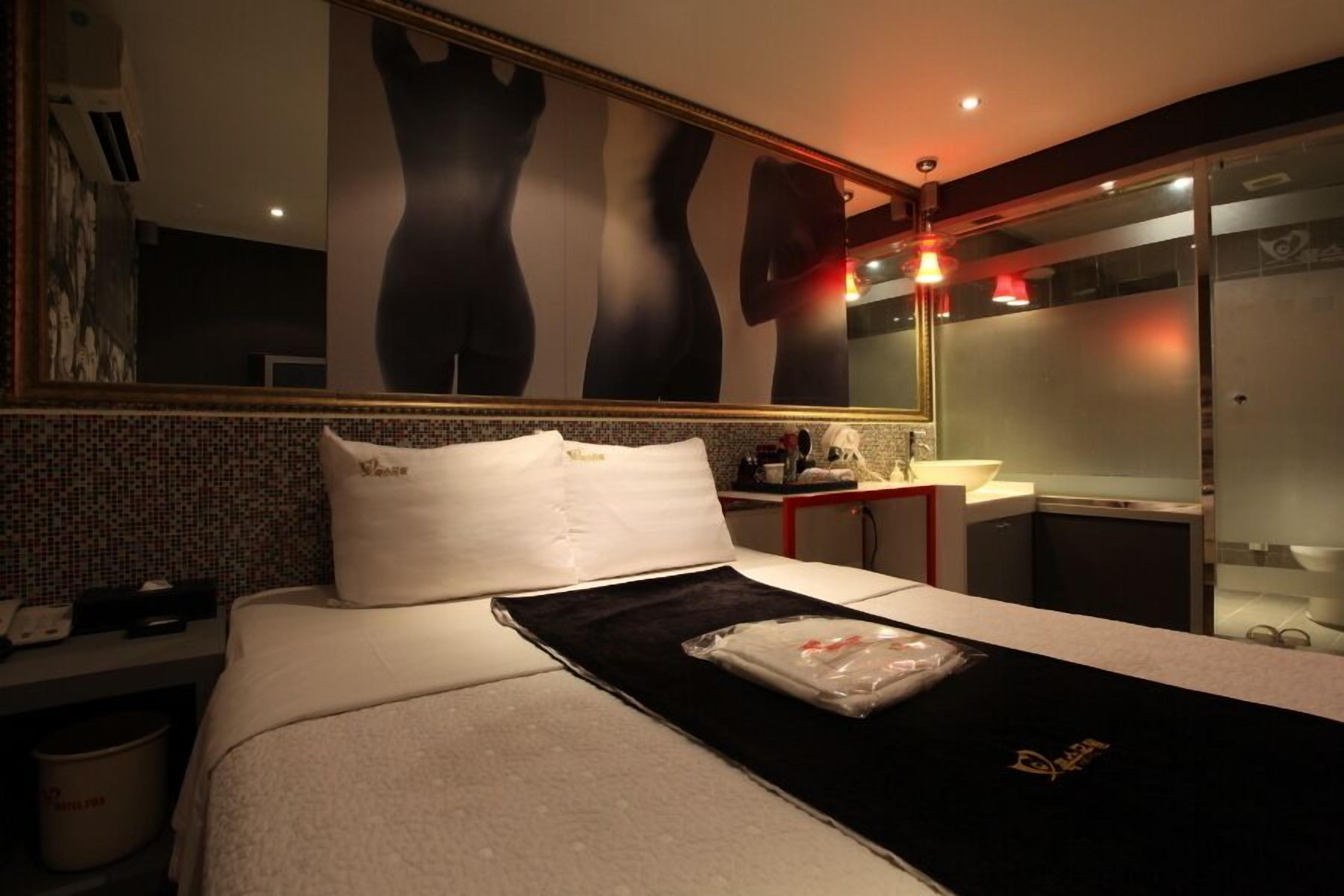 Habitación de hotel con cama, un espejo grande, una mesita y un baño visible a través de una puerta de cristal.