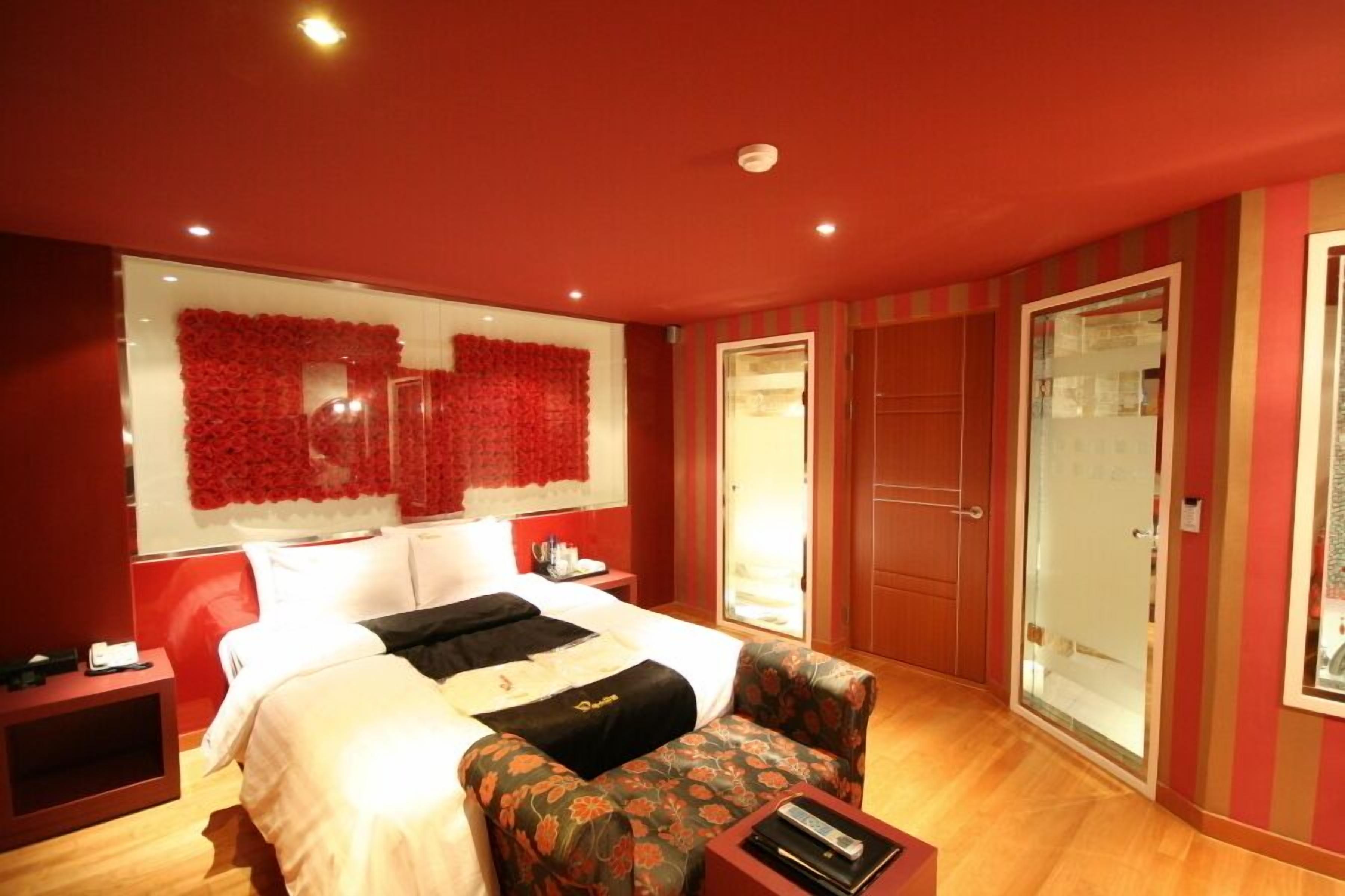 Una habitación de hotel con una cama grande, un pequeño sofá, una mesita de noche y un espejo.