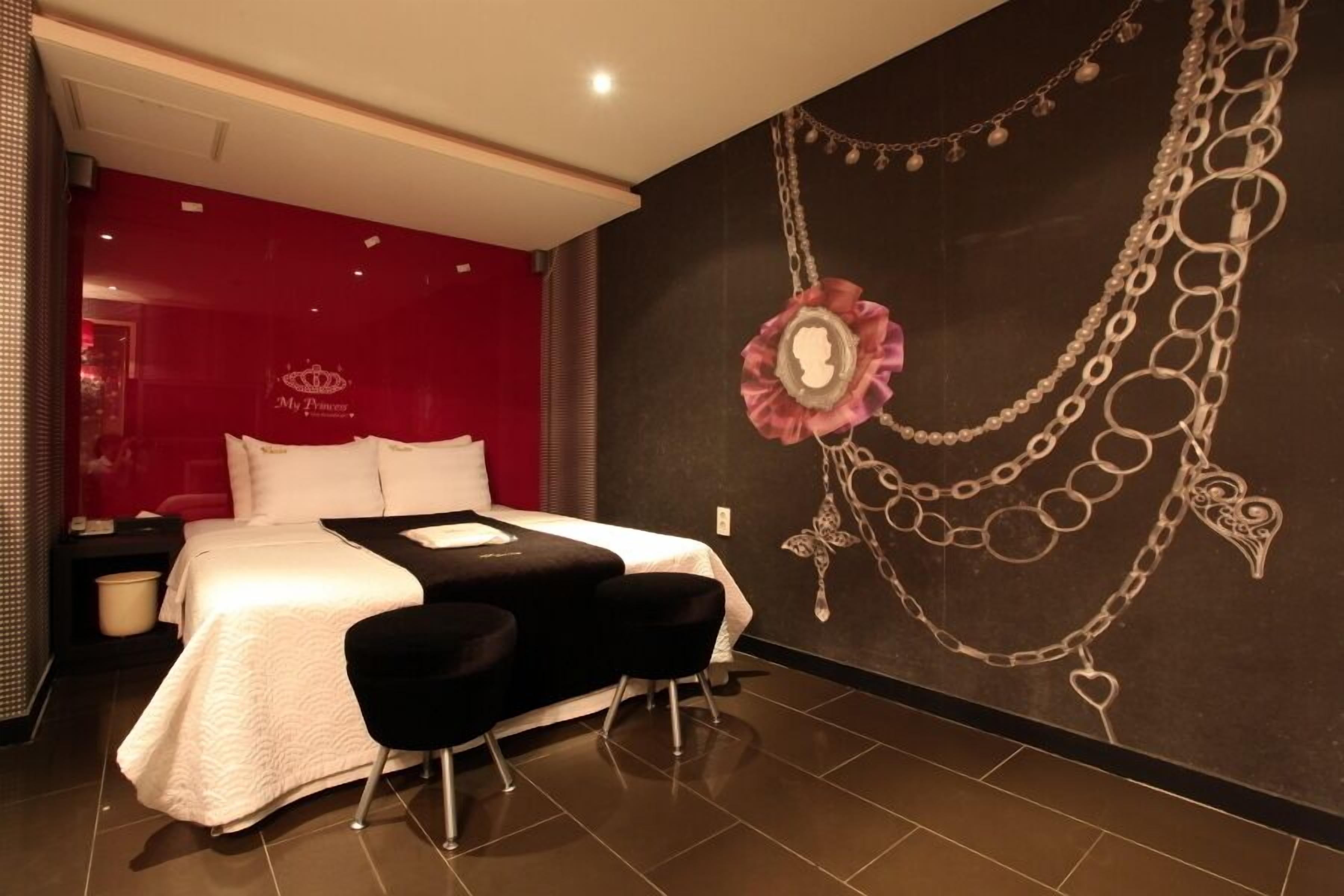 A modern hotel room with a large bed, a black sofa, and a decorative wall with a necklace design.