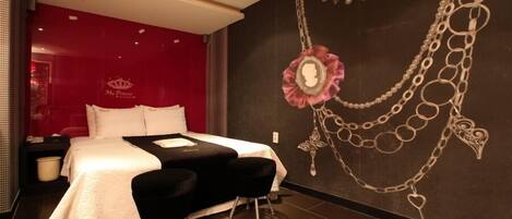 A modern hotel room with a large bed, a black sofa, and a decorative wall with a necklace design.