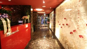Ein Hotel-Empfangsbereich mit einem roten Empfangstresen, Marmorböden und dekorativen Wandelementen.