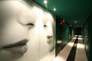 A hallway with a black and white striped floor, green walls, and a large mirrored wall with a partial reflection of a face. - Fox Hotel (Seoul)