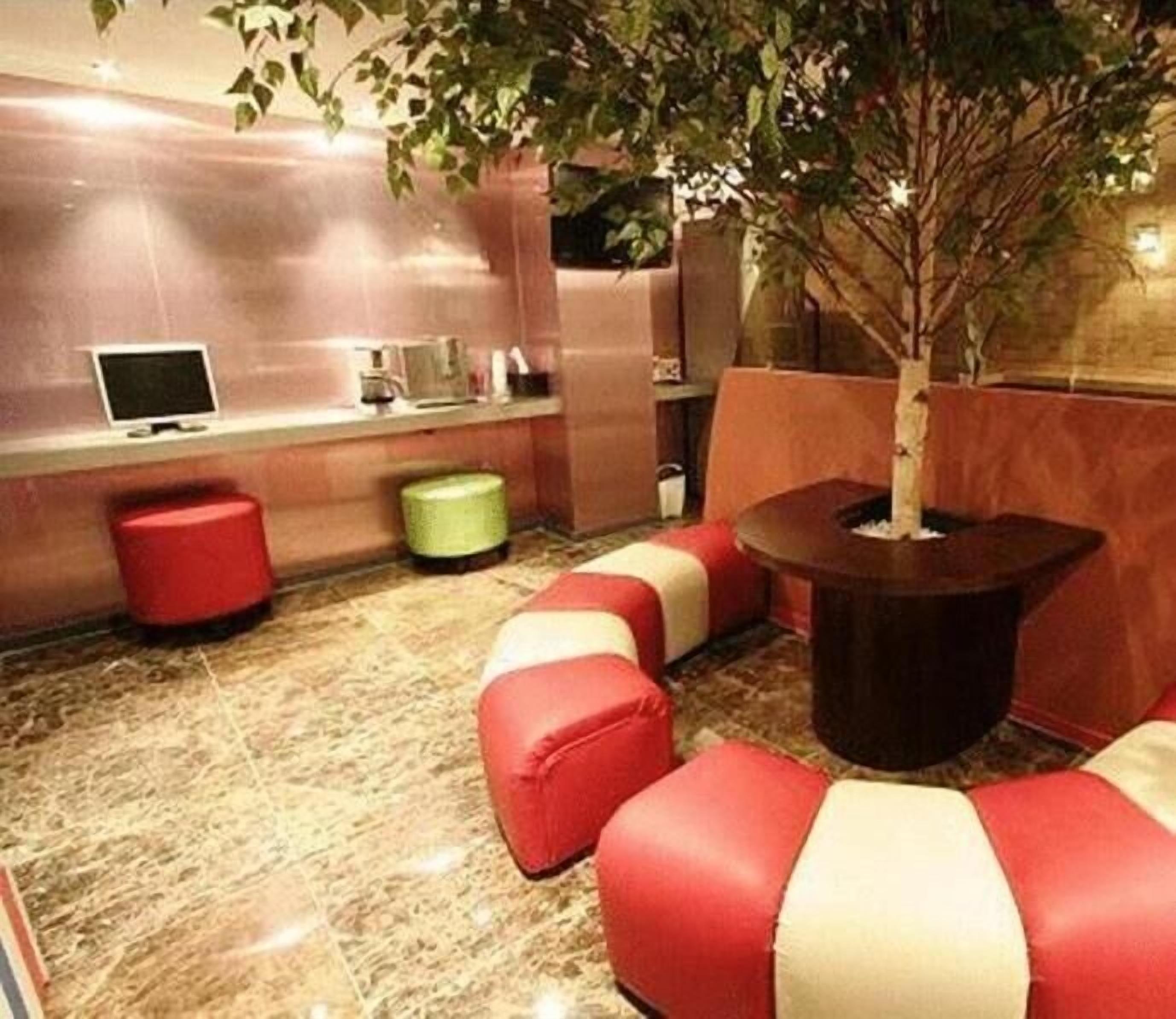 Un área de descanso moderna con asientos acolchados en rojo y blanco, una mesita y una planta en maceta.
