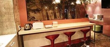 A modern kitchen with a marble countertop, red bar stools, and a large painting on the wall.