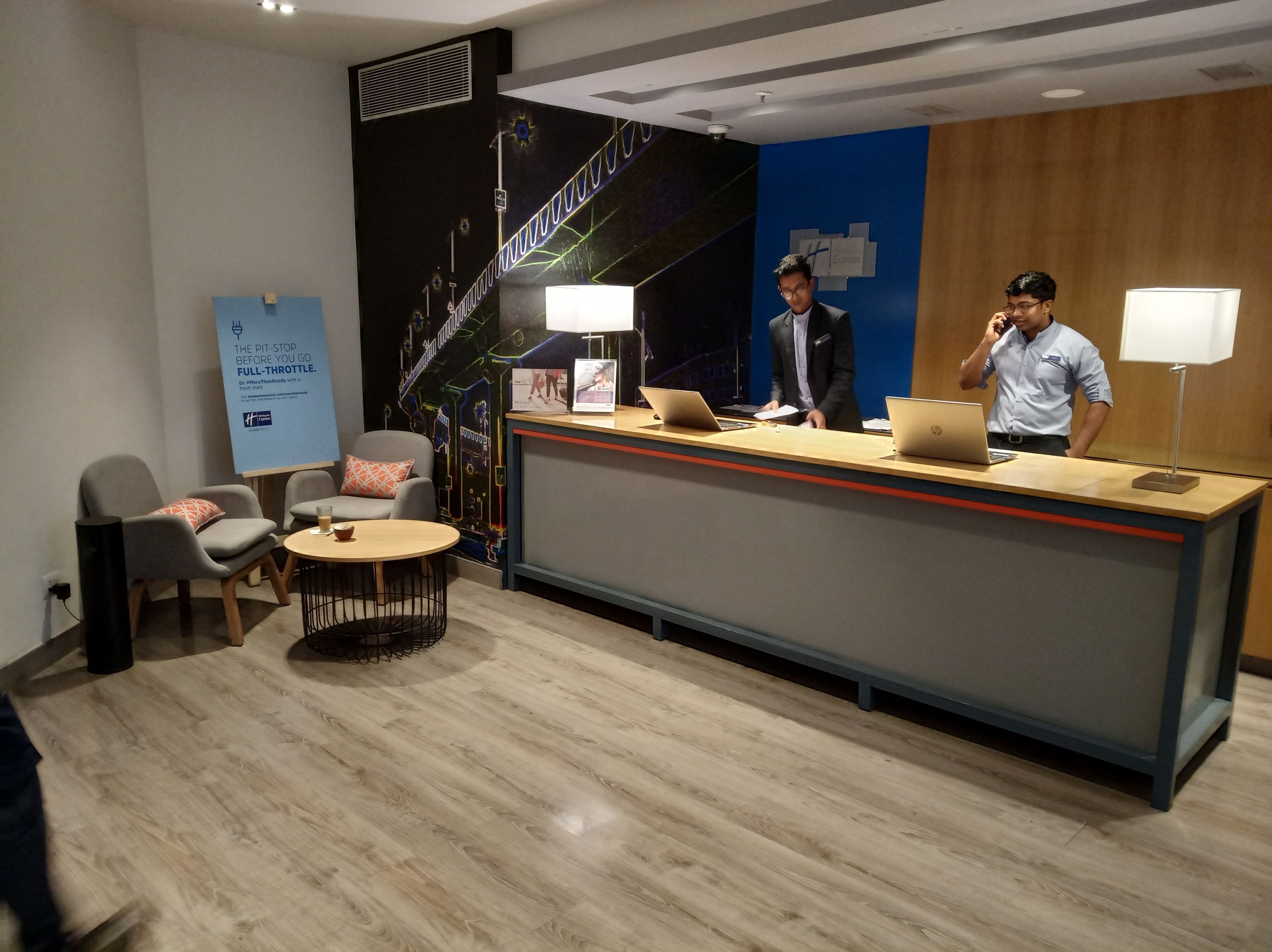 Un área de recepción moderna con un mostrador, dos sillas, una mesita y un mural en la pared.