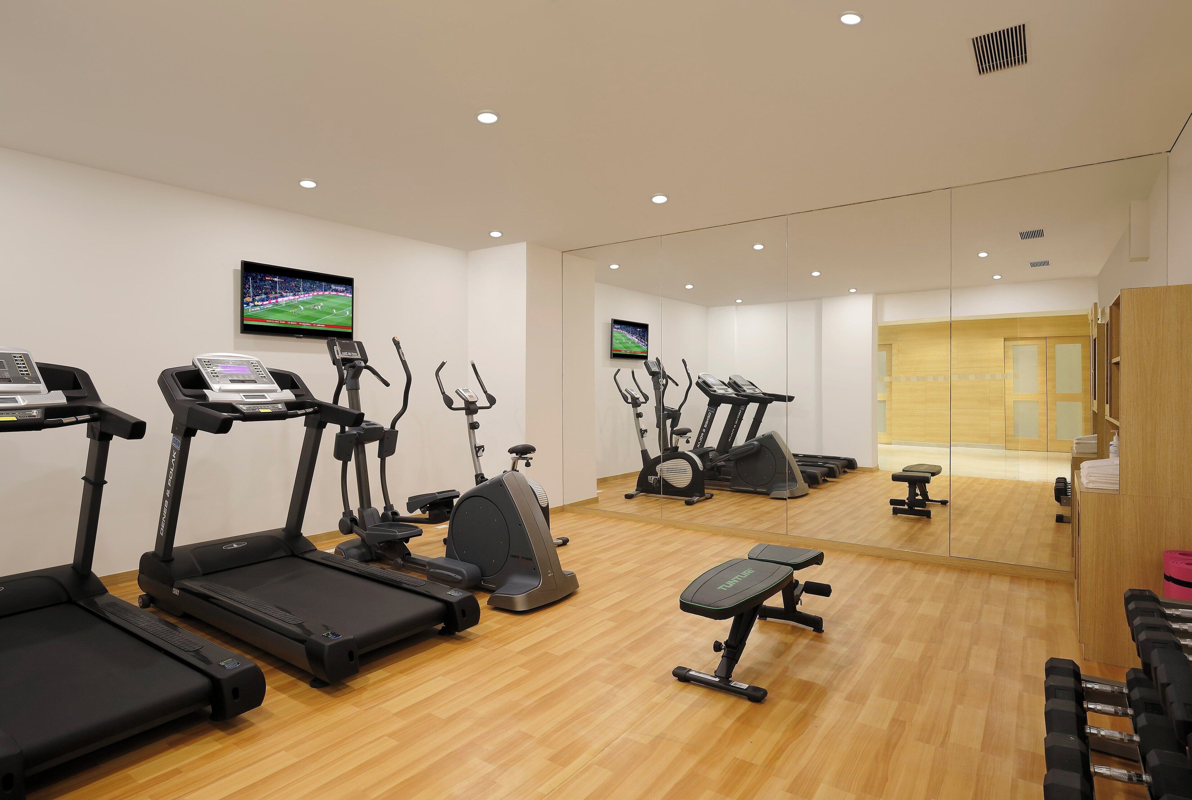 A gym with treadmills, elliptical machines, and a mirrored wall.