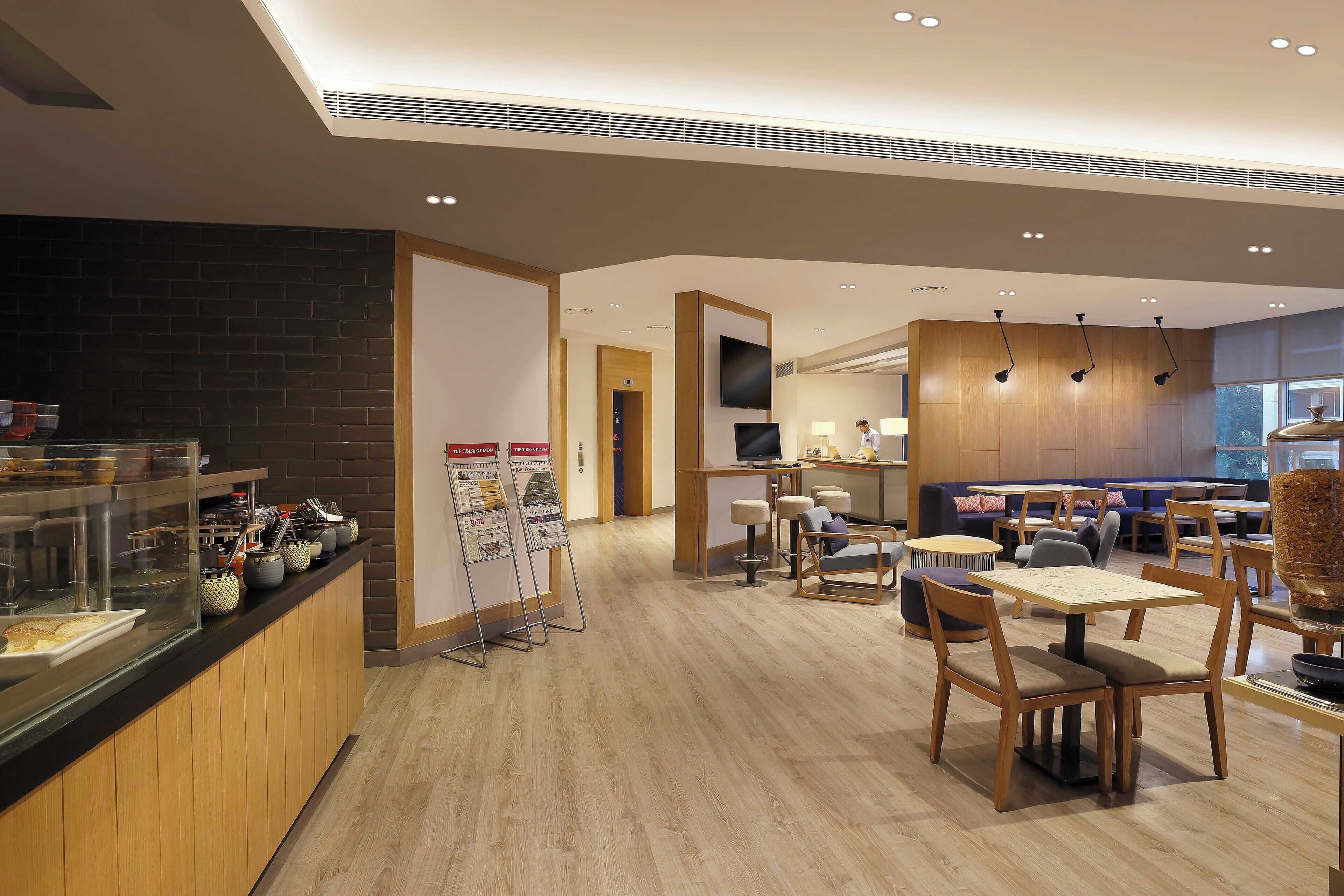 A modern cafe with wooden flooring, a counter with newspapers, and a seating area with tables and chairs.