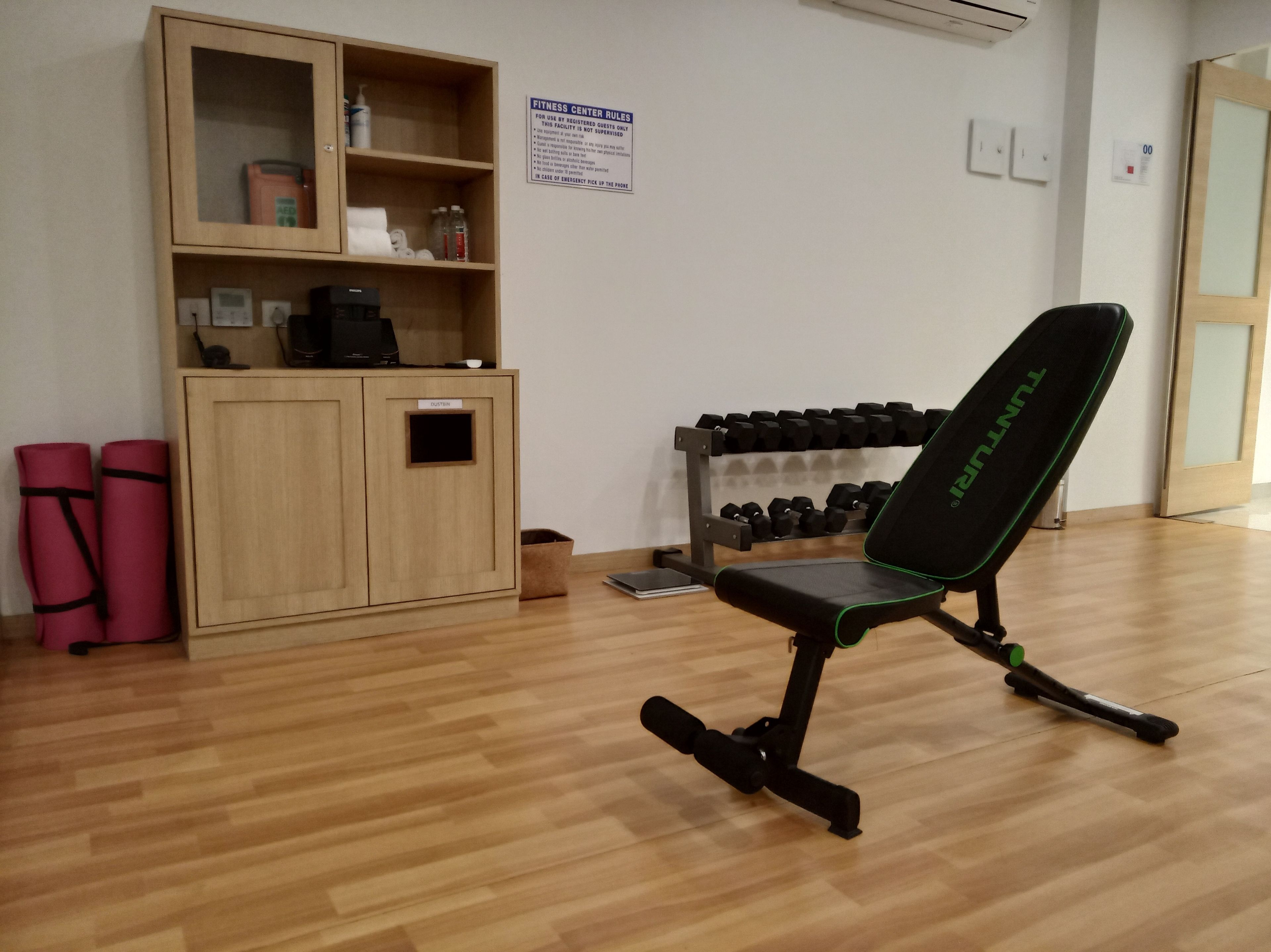 Ett träningscenter med en svart träningsstol, ett ställ med hantlar och ett träskåp med diverse föremål.