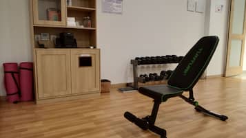 A fitness center with a black exercise chair, a rack of dumbbells, and a wooden cabinet with various items.