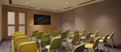 A conference room with rows of chairs, a large flat-screen TV on the wall, and a wooden door.
