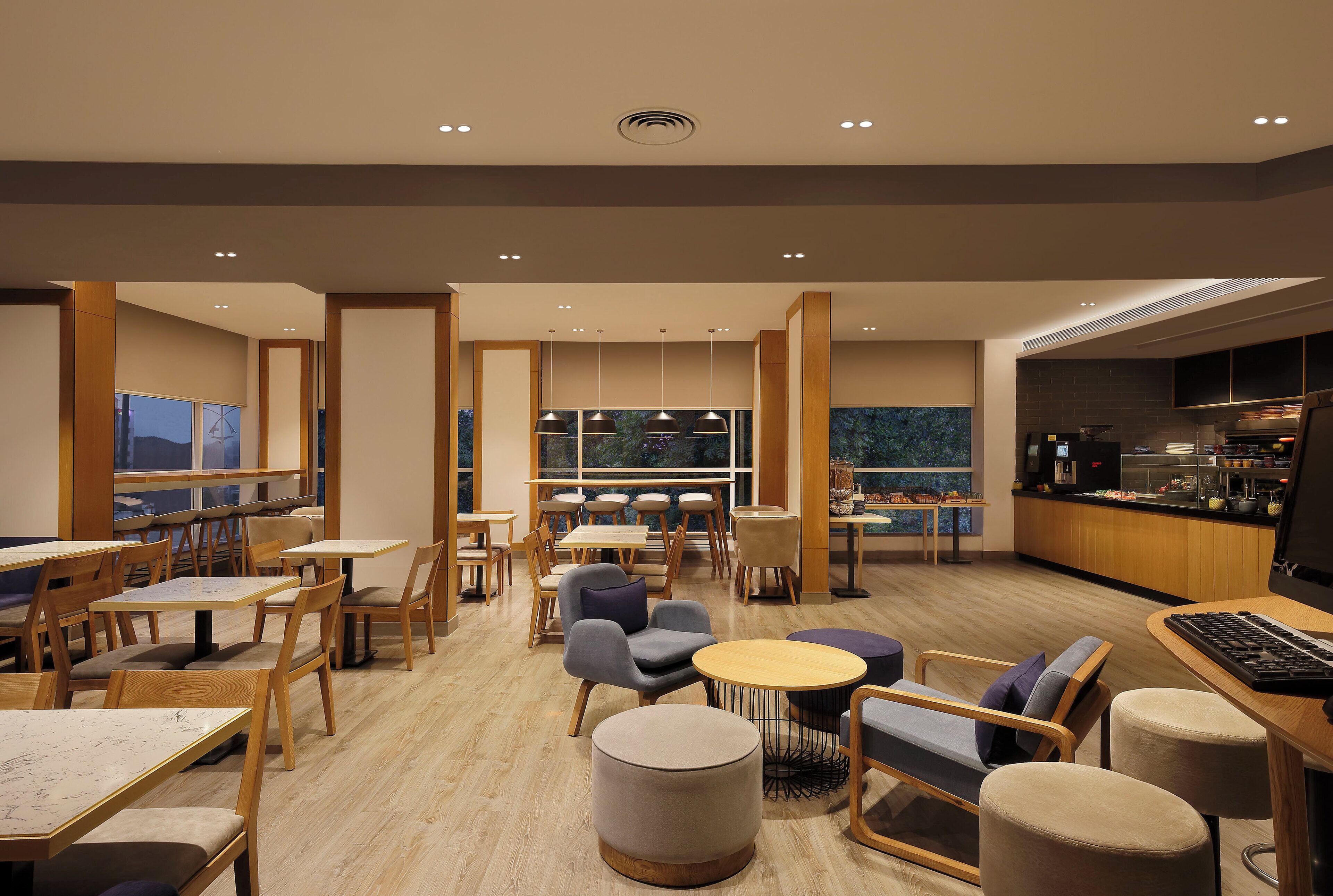 A modern restaurant interior with wooden tables and chairs, a bar area, and large windows offering views.