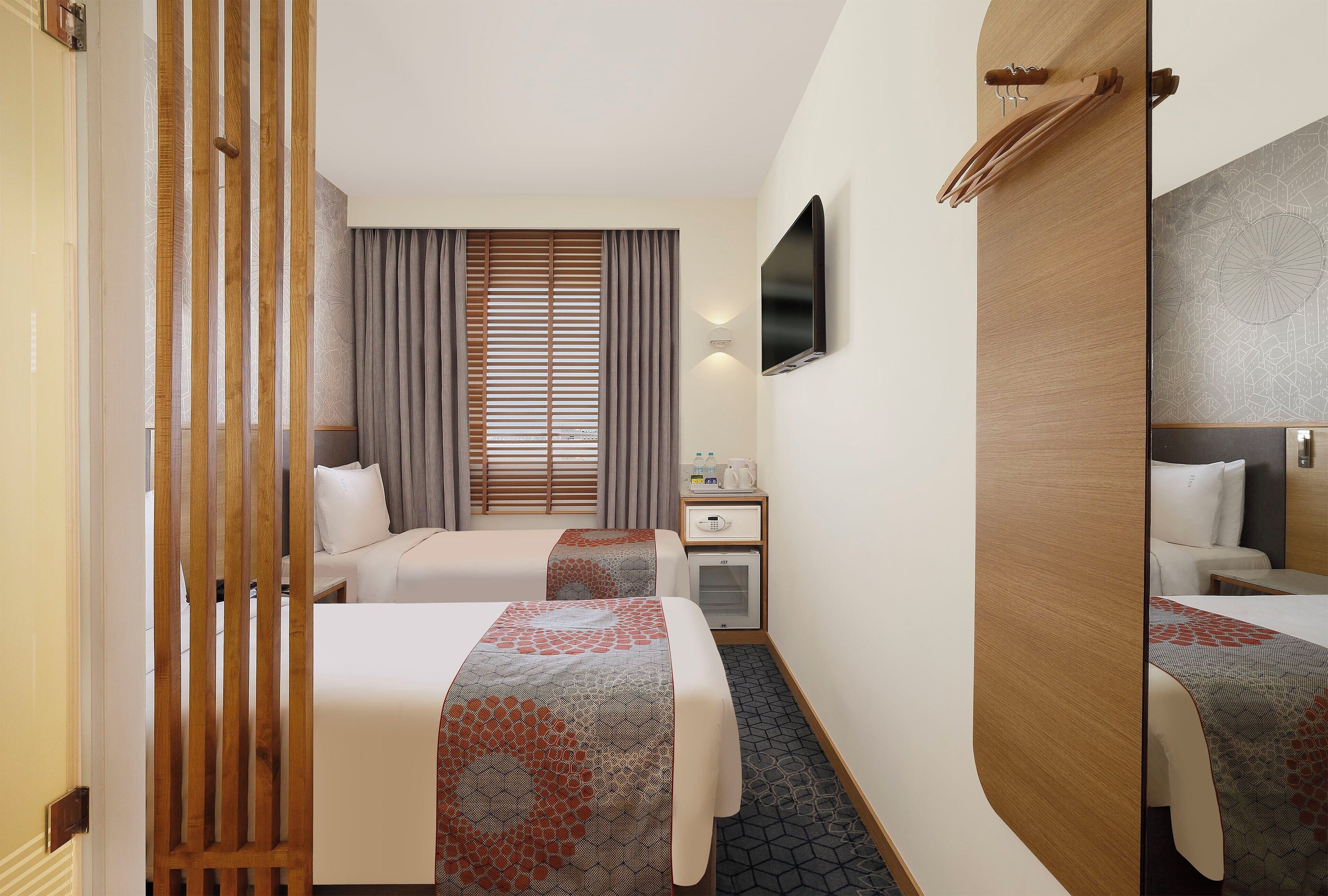 A hotel room with two beds, a desk, a flat-screen TV, and a minibar.