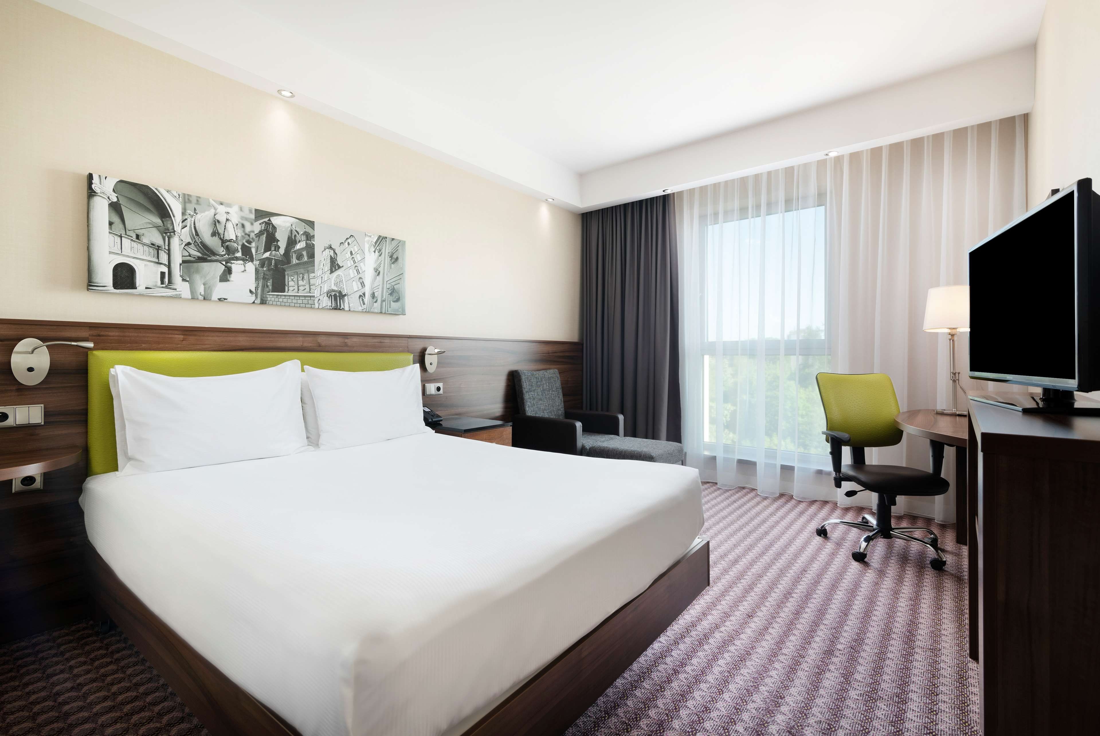 Habitación de hotel con una cama grande, un escritorio con silla, televisor y ventana con cortinas.