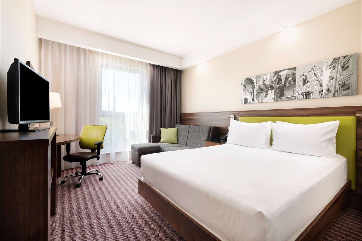 A hotel room with a large bed, a desk with a television, a chair, and a sofa.