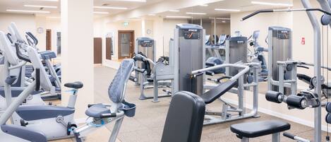 Un gimnasio con diversas máquinas de ejercicio, incluyendo cintas de correr, elípticas y estaciones de pesas.