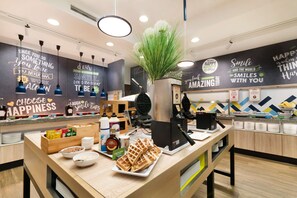 A cafe interior with a counter, waffle display, and motivational wall art. - Hampton by Hilton Krakow (Kraków)
