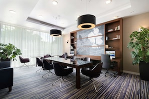 Una sala de conferencias moderna con una mesa de vidrio, sillas negras, una amplia estantería y una pantalla para proyector.