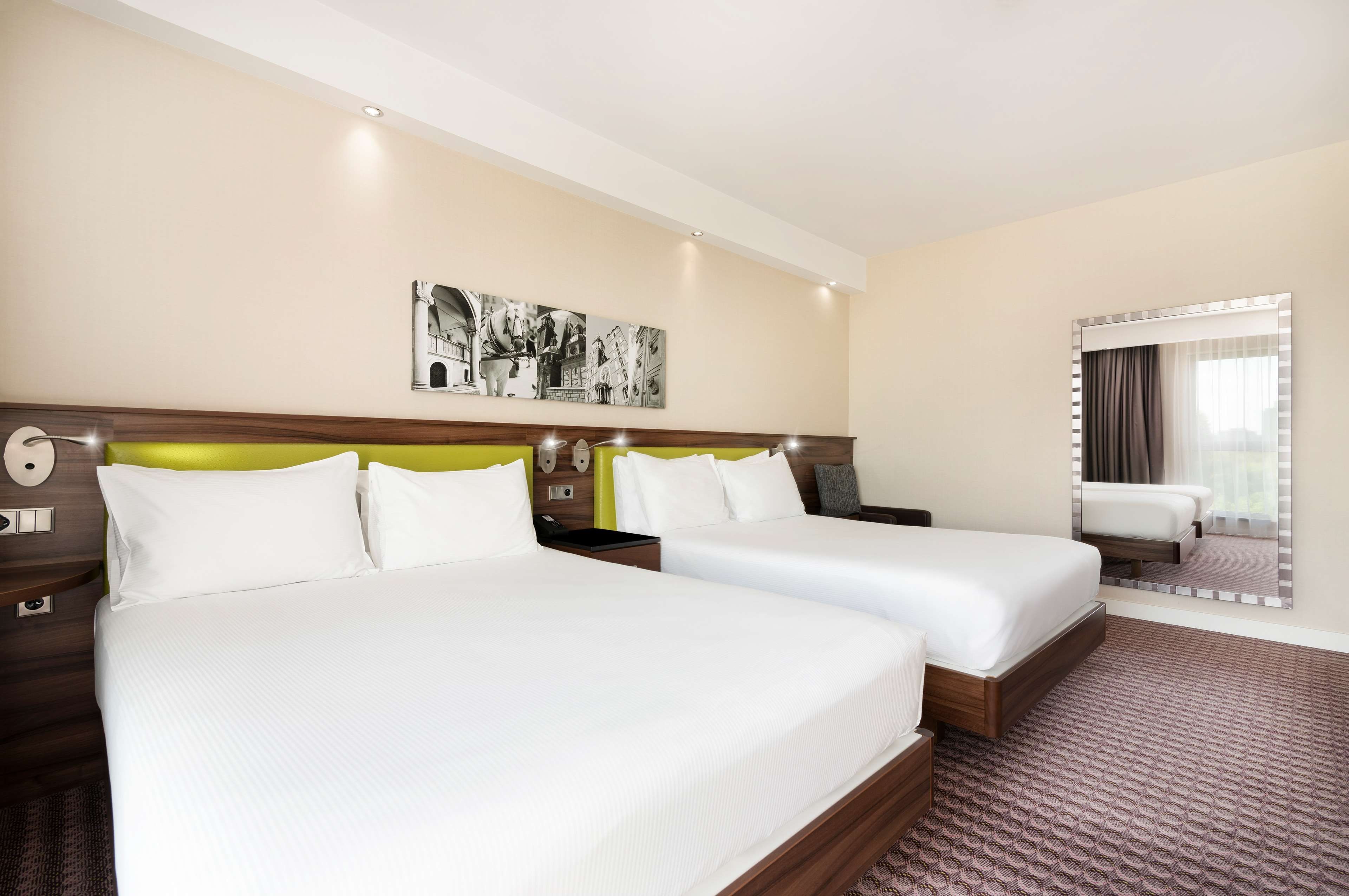 Quarto de hotel com duas camas, um quadro grande pendurado na parede e uma janela com cortinas.
